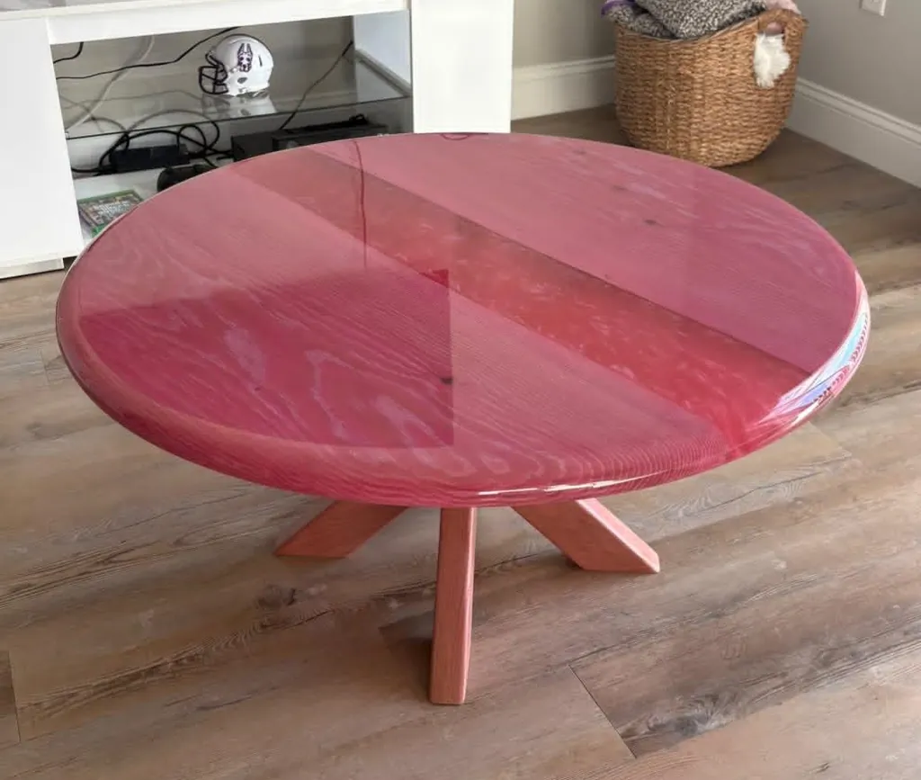 Round coffee table with a glossy pink epoxy top and a crossed wooden base